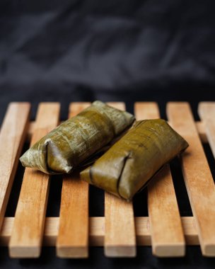 Lepet kek siyah arka planda izole. Kue lepet, yer fıstığıyla karıştırılmış, hindistan cevizi sütüyle pişirilmiş ve muz yapraklarına sarılmış glutinöz pirinçten yapılır. Lepet kek tipik bir Endonezya pastasıdır. Odak bulanıklığı.