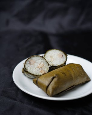 Lepet kek siyah arka planda izole. Kue lepet, yer fıstığıyla karıştırılmış, hindistan cevizi sütüyle pişirilmiş ve muz yapraklarına sarılmış glutinöz pirinçten yapılır. Lepet kek tipik bir Endonezya pastasıdır. Odak bulanıklığı.