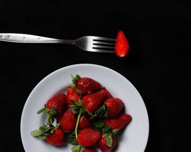 Karanlık arka planda izole edilmiş taze çilekler. Lezzetli tadının yanı sıra, çileklerin bağışıklığı artırmak ve kanseri önlemek gibi vücut için de faydaları var. Çilek modeli..