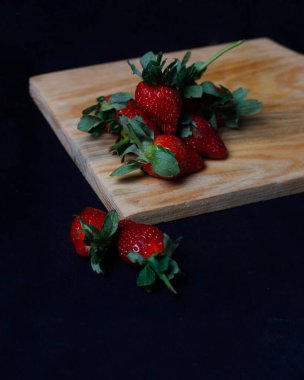 Karanlık arka planda izole edilmiş taze çilekler. Lezzetli tadının yanı sıra, çileklerin bağışıklığı artırmak ve kanseri önlemek gibi vücut için de faydaları var. Çilek modeli..