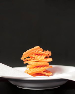 Fırında patates cipsi. Tatlı ve baharatlı kırmızı baharatlara sarılı abur cuburlar patates cipsinin tadını artırır. Atıştırmalık gevrek ve lezzetli patates cipsi. Cips modeli. Odak bulanıklığı.