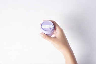 Görüntü, beyaz bir yüzeyde nemlendirici şişeyi tutan bir eli gösteriyor..                        