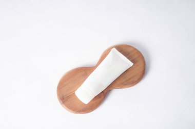 Bir güneş kremi şişesi temiz beyaz bir zemine karşı ahşap bir tabağın üzerinde düzgünce oturur..                            