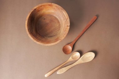 Kahverengi arka plana tahta bir kâse ve tahta bir kaşık yerleştirilir..                              