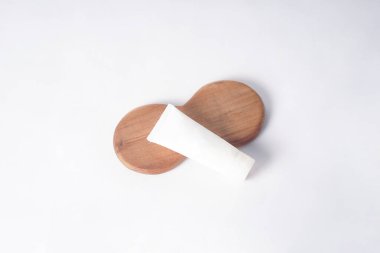 Bir güneş kremi şişesi temiz beyaz bir zemine karşı ahşap bir tabağın üzerinde düzgünce oturur..                            