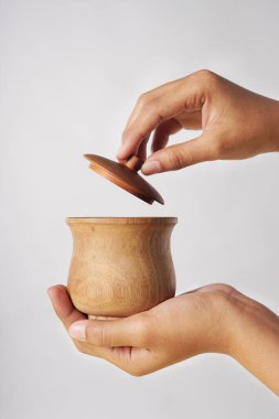 Kapağı beyaz bir arka planda açılırken tahta bir bardak tutuluyor.                               