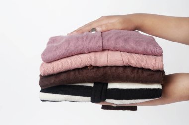 Katlanmış mor, kahverengi, pembe ve siyah-beyaz çizgili elbiseler düzgünce istiflenir ve iki eliyle beyaz arka planda tutulur.                              