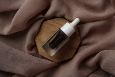 Bir Glad2Glow serumu, kahverengi kumaşla kaplı ahşap bir tepsiye konur. Sıcak ve doğal bir görünüm yaratır.                         