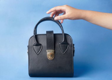 Siyah bir çanta canlı bir mavi arkaplan önünde nazikçe el ele tutulur.      