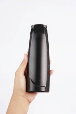 Emeron şampuan şişesi temiz beyaz bir arka planda güvenli bir şekilde elle tutulur.                        