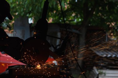 Usta öğütme makinesiyle metali keser. Atölyedeki metalden kıvılcımlar (sığ DOF)