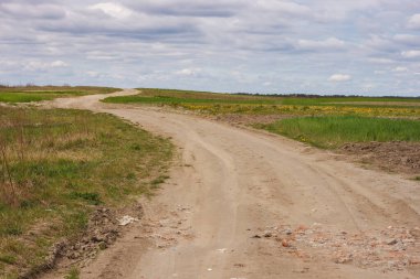 Bulutlu bahar gününe karşı ekili tarlalar arasında toprak yol.
