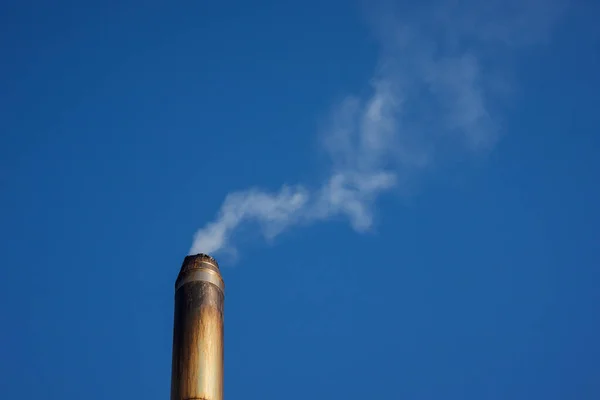 Metal smoke pipe with smoke on blue sky background. Copy space.