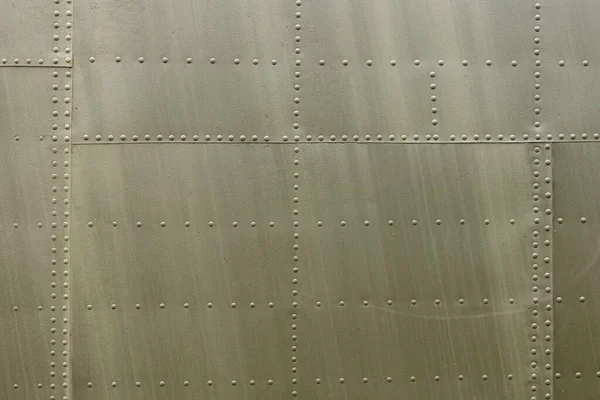 Eski bir uçağın gövdesinin detayları. Eski kamuflaj yüzeyi, pul pul dökülmüş boya ve askeri bir uçağın perçinlenmiş perçinleriyle..