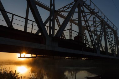 Nehir üzerindeki demiryolu köprüsünün silüeti. Güneşin doğuşu sisli nehirde