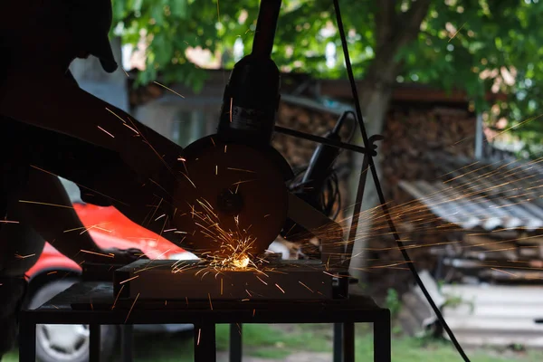 The master cuts the metal with a grinding machine. Sparks from metal in the workshop (shallow DOF)