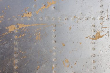 Eski bir uçağın gövdesinin detayları. Eski kamuflaj yüzeyi, pul pul dökülmüş boya ve askeri bir uçağın perçinlenmiş perçinleriyle..