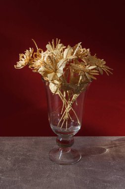Kırmızı arka planda samandan yapılmış bir buket çiçekli cam bir vazo.