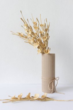 Çiçekler mukavva bir vazoda beyaz bir zemin üzerinde samandan yapılmıştır.