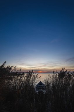 Gölde gün batımı. Eski kırsal ahşap, gölün sığ sularına demirlenmiş balıkçı teknesi. Parça. DOF