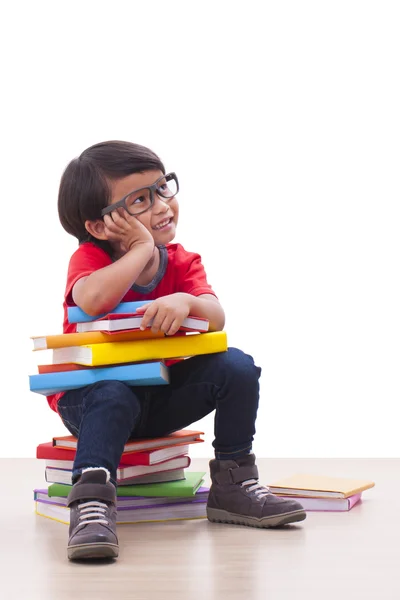 Mignon garçon tenant un livre tout en étant assis sur des livres — Photo