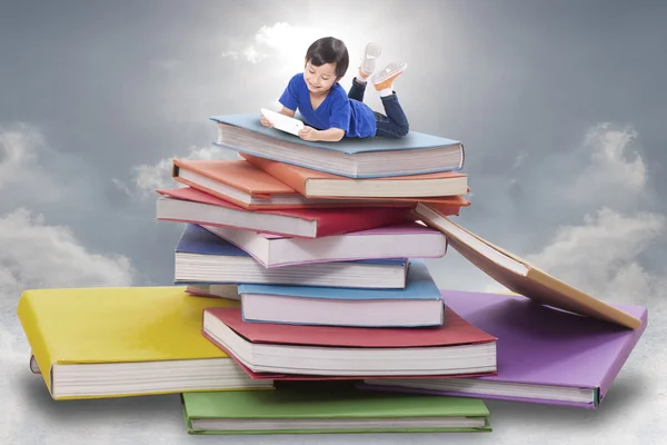 Menino jogando tablet e sentado em pilha de livros — Fotografia de Stock