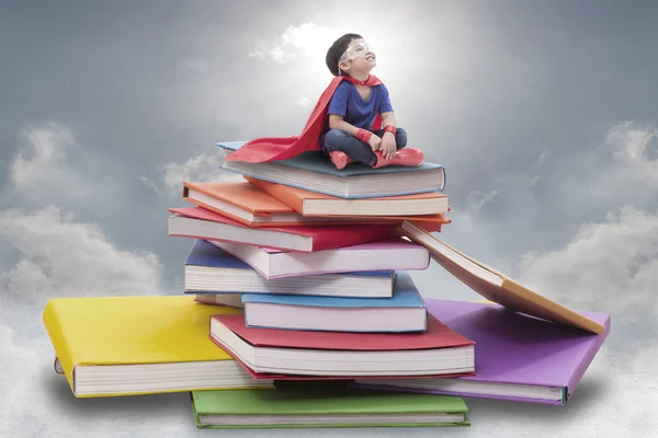 Superhero boy child sitting on pile of books