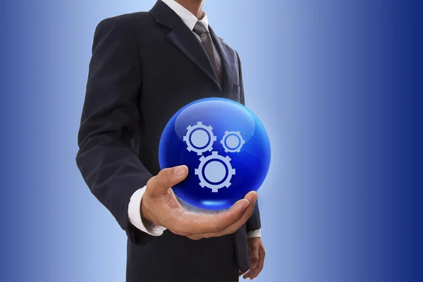 Businessman hand holding blue crystal ball with gears symbol. — Stock Photo, Image