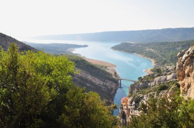 A deep canyon of white rocks overgrown with green grass over a turquoise blue river