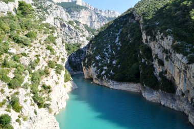 A deep canyon of white rocks overgrown with green grass over a turquoise blue river