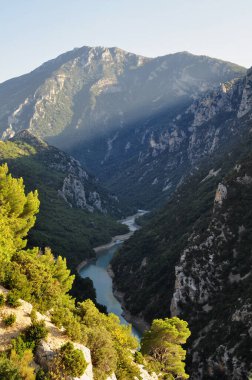 A deep canyon of white rocks overgrown with green grass over a turquoise blue river