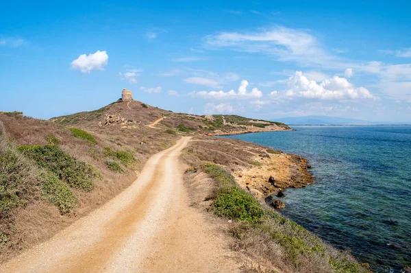 Arka planda eski bir kulesi olan deniz kenarındaki kumlu yol.