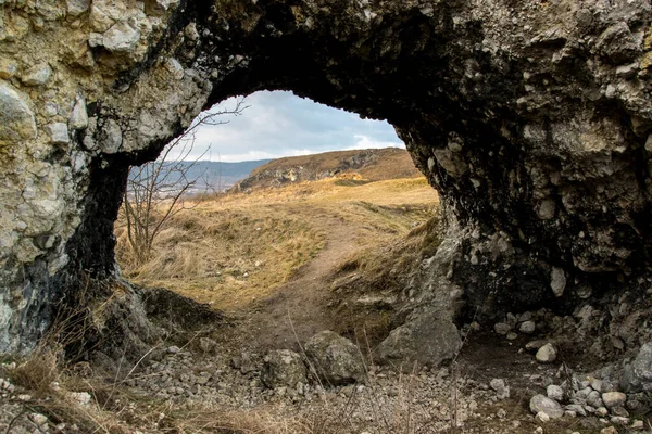 View of the autumn sunlit landscape through a tunnel created from rocks