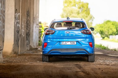 Brno, Çek Cumhuriyeti - 18 Haziran 2025: Elektrikli motorlu mavi şehir SUV Ford Puma gen-e. Ekolojik sürüş için batarya ile küçük bir kesişme. Araba otoban köprüsünün altında park halinde..