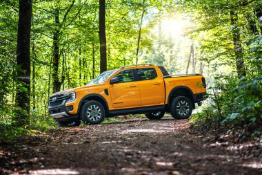 Brno, Çek Cumhuriyeti - 22 Eylül 2025: Sarı Ford Ranger Wildtrack PHEV off-road kamyonet doğada duruyor. Ağaçların arasında orman yolunda bir cesetle birlikte büyük bir off-road hibrit araba..
