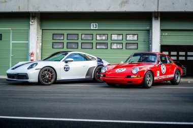 Brno, Czech Republic - October 10, 2025: Two sports Porsches, one old from 1969 and the other new from 2023, stand in front of the pits on the race track. Old and new fast car.