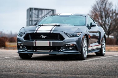 Brno, Çek Cumhuriyeti - 31 Aralık 2023: Gri Amerikan spor otomobili Ford Mustang açık otoparkta duruyor. Beyaz çizgili araba, folyo etiketli. Hızlı araba ön görünümü.