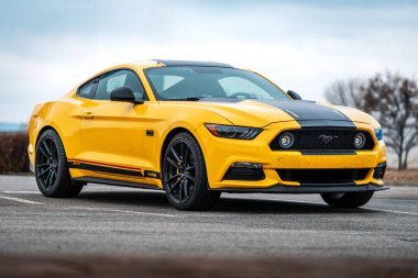 Brno, Çek Cumhuriyeti - 31 Aralık 2023: Sarı Amerikan spor arabası Ford Mustang dışarıda park alanında duruyor. Siyah çizgili araba, folyo etiketli. Ön taraftan hızlı bir araba..