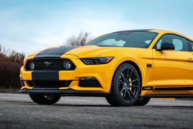 Brno, Çek Cumhuriyeti - 31 Aralık 2023: Sarı Amerikan spor arabası Ford Mustang dışarıda park alanında duruyor. Siyah çizgili araba, folyo etiketli. Ön taraftan hızlı bir araba..