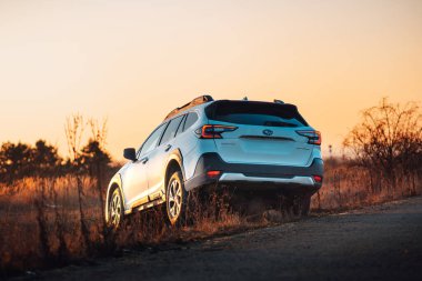 Brno, Çek Cumhuriyeti - 10 Şubat 2026: Beyaz Subaru Outback SUV, kışın gün batımında bir arazide. Akşamları gökyüzü turuncu ışıkla aydınlatılıyor. Japon bir jiple..