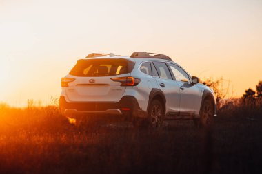 Brno, Çek Cumhuriyeti - 10 Şubat 2026: Japon off-road otomobili Subaru Outback doğada kışın gün batımında bir arazide duruyor. Yolculukta beyaz bir SUV 'a radyasyon.