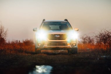 Brno, Çek Cumhuriyeti - 10 Şubat 2026: Beyaz Subaru Outback SUV, kışın gün batımında bir arazide. Akşamları gökyüzü turuncu ışıkla aydınlatılıyor. Japon bir jiple..