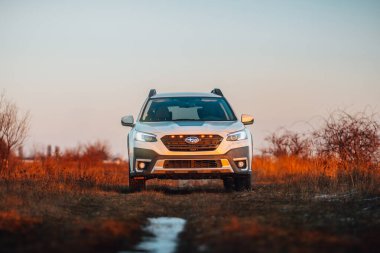 Brno, Çek Cumhuriyeti - 10 Şubat 2026: Beyaz Subaru Outback SUV, kışın gün batımında bir arazide. Akşamları gökyüzü turuncu ışıkla aydınlatılıyor. Japon bir jiple..