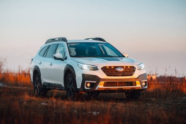Brno, Çek Cumhuriyeti - 10 Şubat 2026: Beyaz Subaru Outback SUV, kışın gün batımında bir arazide. Akşamları gökyüzü turuncu ışıkla aydınlatılıyor. Japon bir jiple..