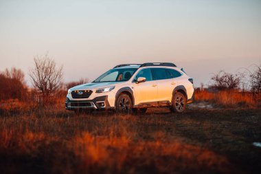 Brno, Çek Cumhuriyeti - 10 Şubat 2026: Beyaz Subaru Outback SUV, kışın gün batımında bir arazide. Akşamları gökyüzü turuncu ışıkla aydınlatılıyor. Japon bir jiple..