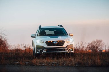 Brno, Çek Cumhuriyeti - 10 Şubat 2026: Beyaz Subaru Outback SUV, kışın gün batımında bir arazide. Akşamları gökyüzü turuncu ışıkla aydınlatılıyor. Japon bir jiple..