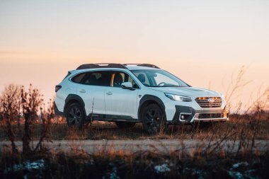 Brno, Çek Cumhuriyeti - 10 Şubat 2026: Beyaz Subaru Outback SUV, kışın gün batımında bir arazide. Akşamları gökyüzü turuncu ışıkla aydınlatılıyor. Japon bir jiple..