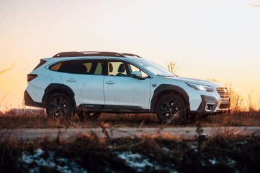 Brno, Çek Cumhuriyeti - 10 Şubat 2026: Beyaz Subaru Outback SUV, kışın gün batımında bir arazide. Akşamları gökyüzü turuncu ışıkla aydınlatılıyor. Japon bir jiple..