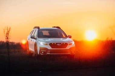 Brno, Çek Cumhuriyeti - 10 Şubat 2026: Subaru Outback 2.5 in white. Japon cipi kışın gün batımında bir çayırda. Aile büyüklüğünde bir araba, doğa gezisinde..