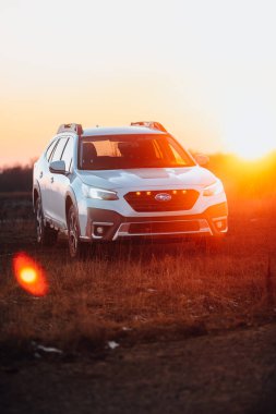 Brno, Çek Cumhuriyeti - 10 Şubat 2026: Japon off-road otomobili Subaru Outback doğada kışın gün batımında bir arazide duruyor. Yolculukta beyaz bir SUV 'a radyasyon.